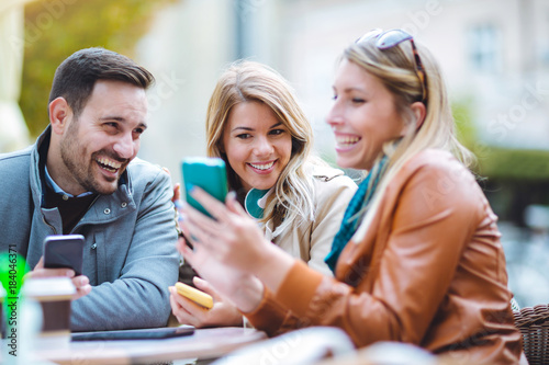 Group of three friends using phone in outdoor cafe on sunny day