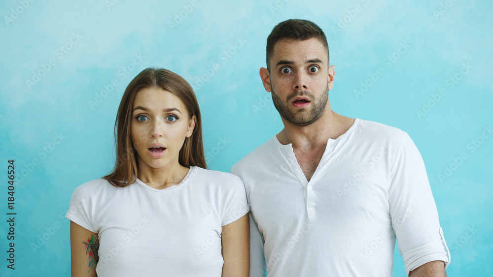 Portrait of young couple actively surprising and wondering looking into camera on blue background