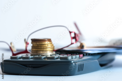 Coins on calculator, eyeglass, pencil, conceptual image of increasing taxes isolated on white background.