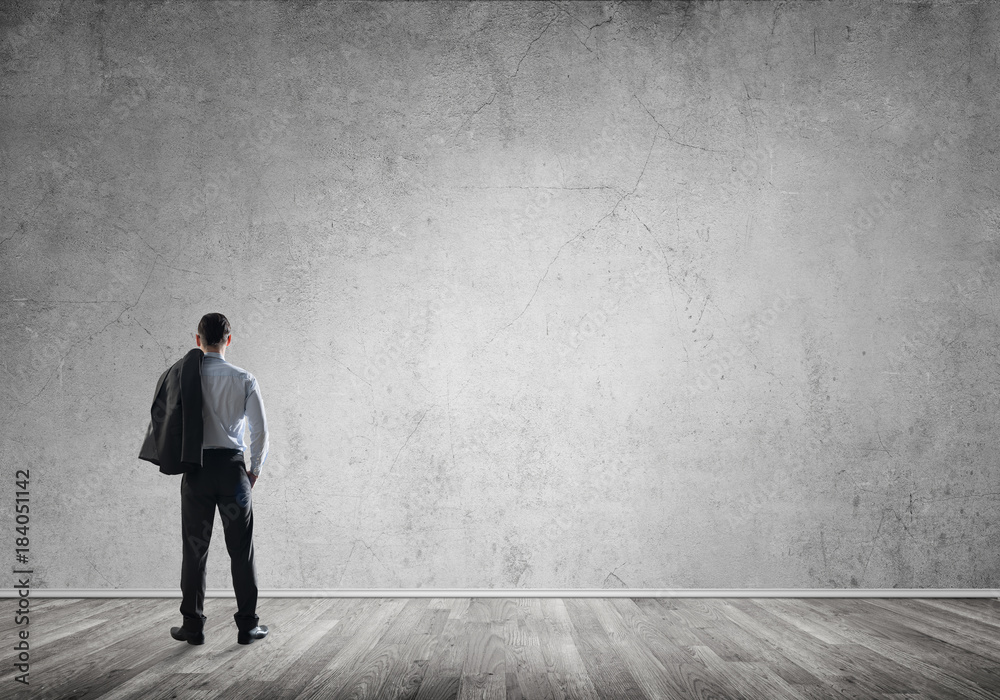 Businessman threw his jacket over his back and looking at blank concrete wall Businessman threw his jacket over his back and looking at blank concrete wall