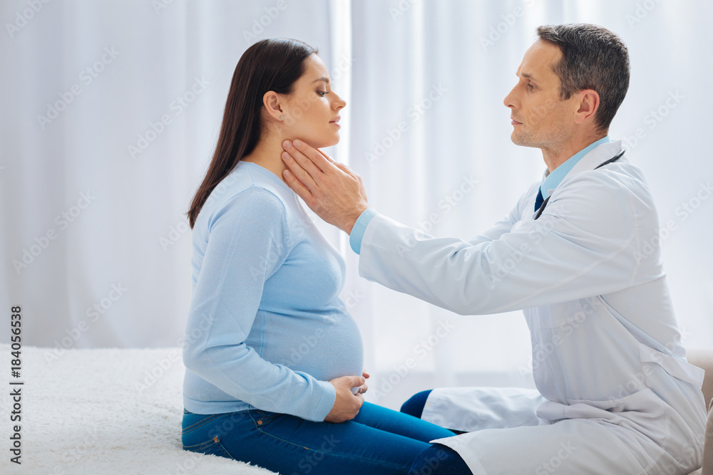 Need to check. Cheerful brunette sitting in semi position and touching her tummy while looking at her specialist Need to check. Cheerful brunette sitting in semi position and touching her tummy while looking at her specialist