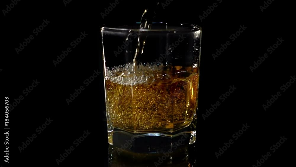 Whiskey is poured into a glass in slow motion on a black background Whiskey is poured into a glass in slow motion on a black background