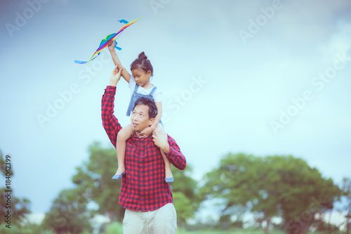 Asian child girl and father with a kite running and happy on meadow in summer in nature