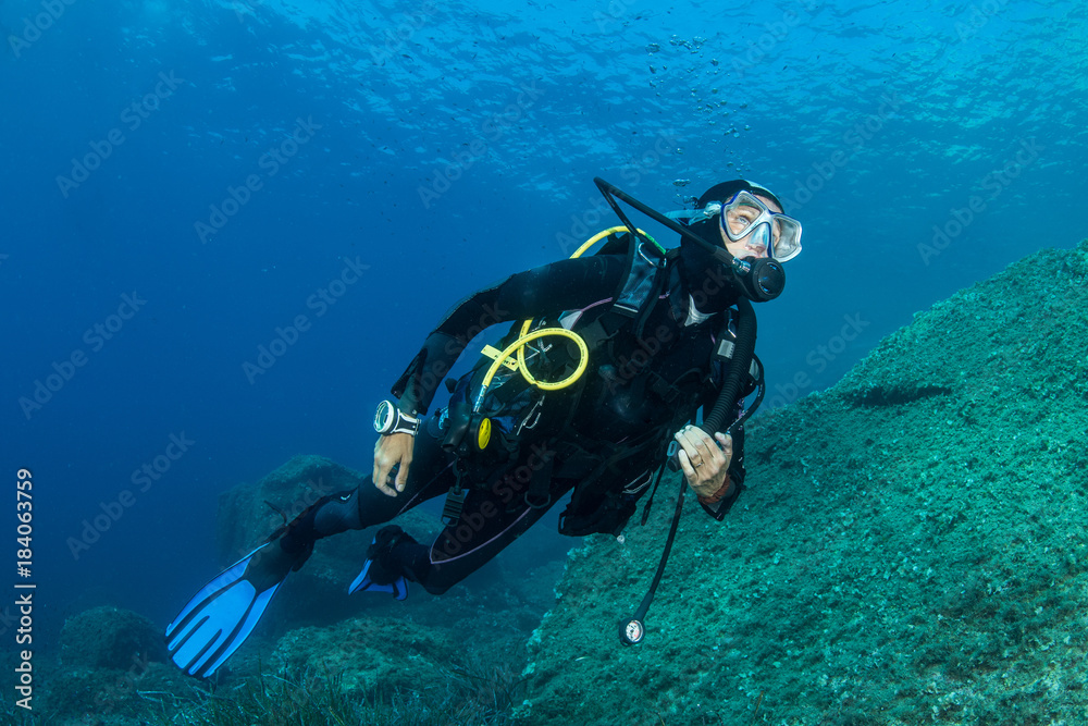 woman scuba diving over rocks in the Mediterranean Sea woman scuba diving over rocks in the Mediterranean Sea