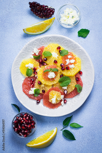 Healthy citrus pomegranate feta salad on light blue background. Top view, space for text.