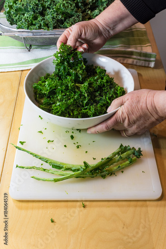 Woman's hand holding up freshly massaged kale greens in a bowl, vertical aspect