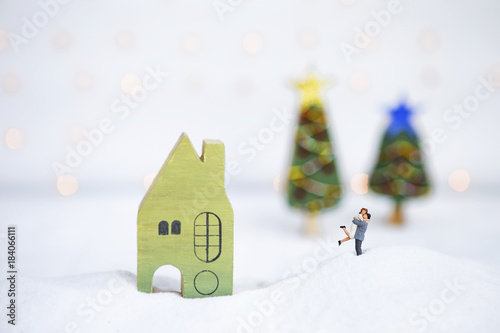 Happy couple with wooden green house on white snow over blurred Christmas tree on white background