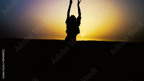 Pretty sexy girl dances in desert with sun on background. Happy beautiful woman is dancing east dance at sunset. Dancer melts, dissolves in sunset