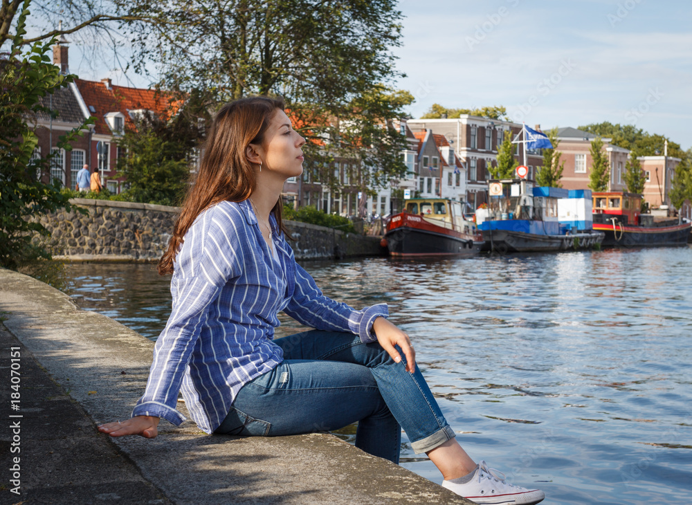 Φωτογραφία Beautiful young woman sitting on the banks of the canal enjoying the scenic views of European cities