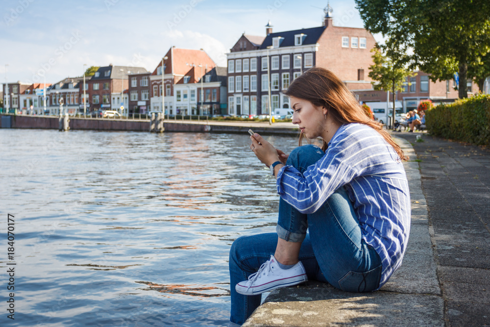 Young woman with mobile phone sitting on the banks of the canal.