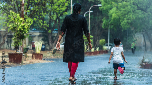 Tableau sur toile Mother and daughter welcoming the first monsoon showers by playing in heavy rain