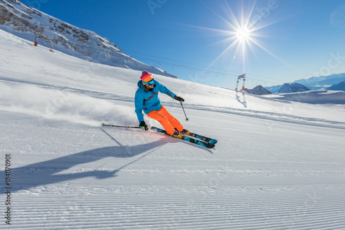 Skier on piste running downhill in Alpine landscape.