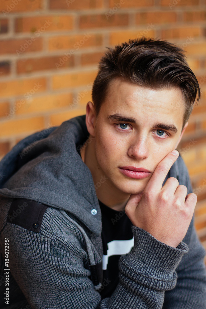 Portrait of young handsome man sitting with brick wall in the background Portrait of young handsome man sitting with brick wall in the background