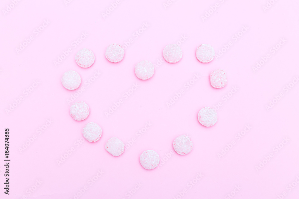 Pink candies are lined in the shape of a heart on a pink background. Flat lay