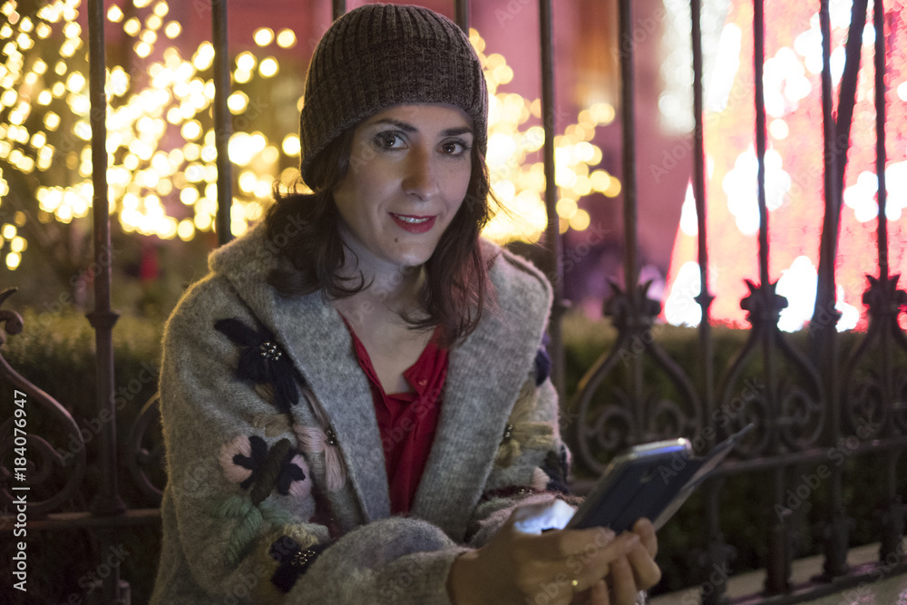 Woman in night christmas scene looking smartphone screen sending christmas greetings Woman in night christmas scene looking smartphone screen sending christmas greetings