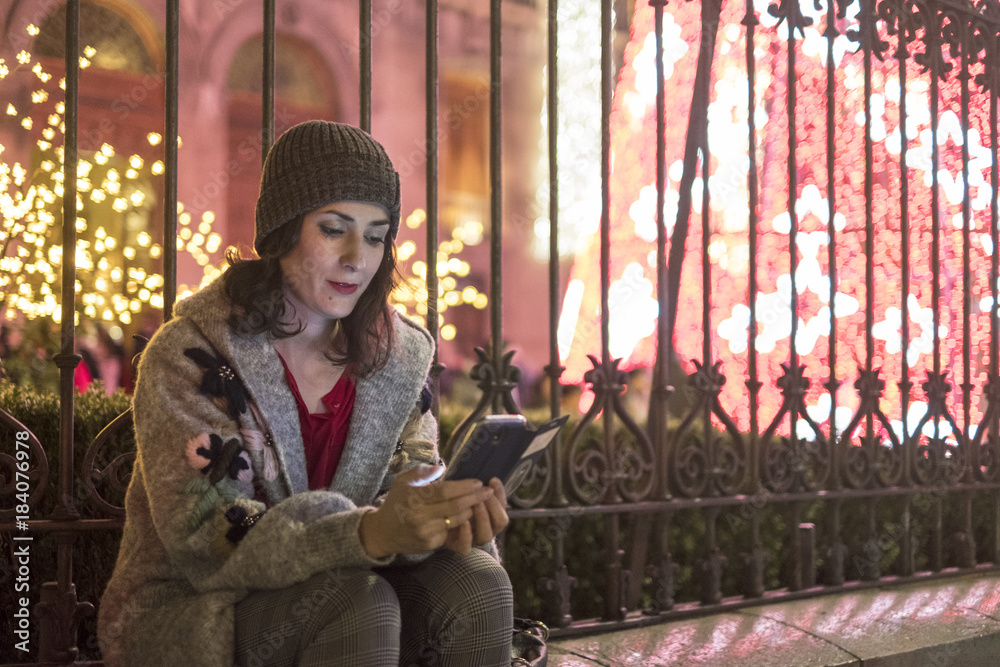 Woman in night christmas scene looking smartphone screen and sending messages