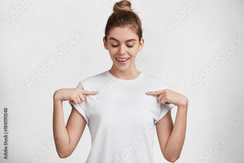 Horizontal shot of glad delightful female dressed in casual t shirt, indicates with fore fingers at blank space, being satisfied with new purchase. Advertising, clothing, people and design concept