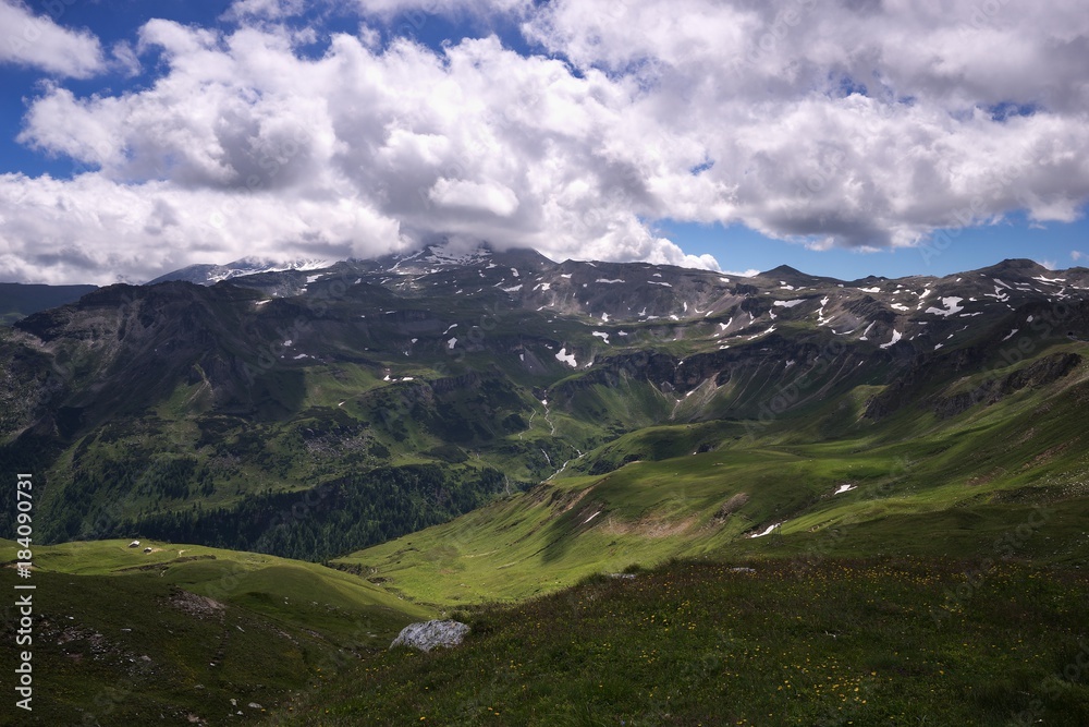Panoramatic Picture of the high positioned large valley with beautifull mountain meadows with blooming flowers in Austian alpine region with peaks still partly covered by snow on the skyline.