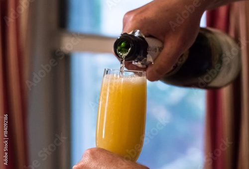 Person pouring champagne into mimosa cocktail