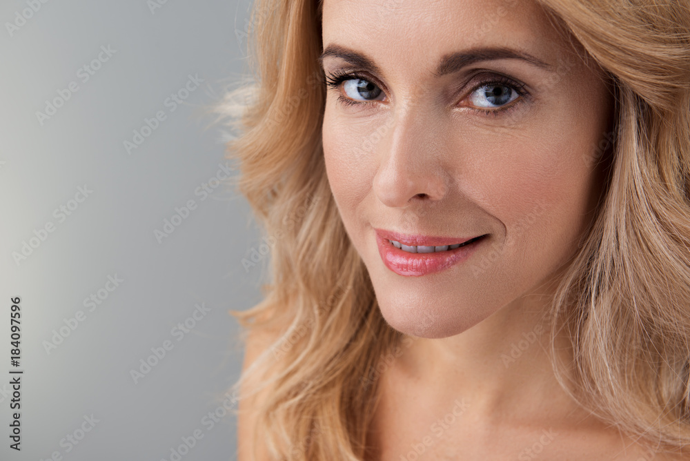 Close-up of face of attractive cheerful middle-aged woman with long hair is standing and looking at camera with joy. Isolated background with copy space in the left side Close-up of face of attractive cheerful middle-aged woman with long hair is standing and looking at camera with joy. Isolated background with copy space in the left side