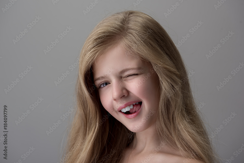 Playful mood. Cheerful coquettish little girl is showing tongue and winking while expressing gladness. Isolated background Playful mood. Cheerful coquettish little girl is showing tongue and winking while expressing gladness. Isolated background