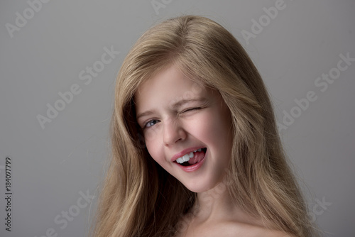 Playful mood. Cheerful coquettish little girl is showing tongue and winking while expressing gladness. Isolated background