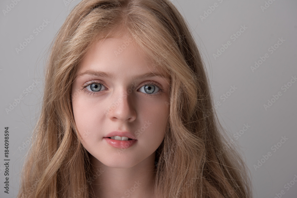 Close-up portrait of pleasant pretty little girl is looking at camera dreamily. Isolated background Close-up portrait of pleasant pretty little girl is looking at camera dreamily. Isolated background