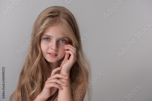 Portrait of positive pretty little girl is looking at camera with smile while standing and touching her face. Isolated background with copy space in the right side