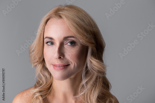 Close-up portrait of gorgeous middle-aged naked woman. She is looking at camera thoughtfully. Isolated background