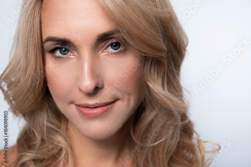 Close-up portrait of gorgeous charming middle-aged woman with fresh skin and long hair. She is looking at camera with slight smile. Isolated background