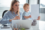 Portrait of uneasy mother and happy kid looking at paper while holding it in hand in modern office. Job and baby concept