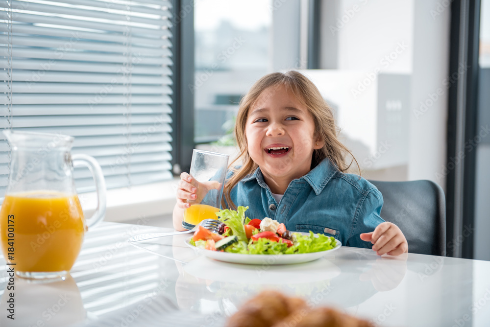 Portrait of cheerful female kid having healthy breakfast at home. She is looking aside with excitement and smiling Portrait of cheerful female kid having healthy breakfast at home. She is looking aside with excitement and smiling