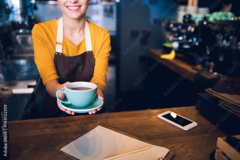 Here is your order. Close up arms of outgoing girl keeping cup of delicious hot tea while standing at counter in cafe. Job concept