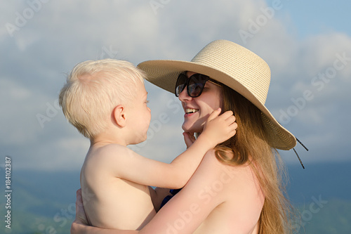 Mom holds a small son in her arms and smiles. Beach, hat, sunny day