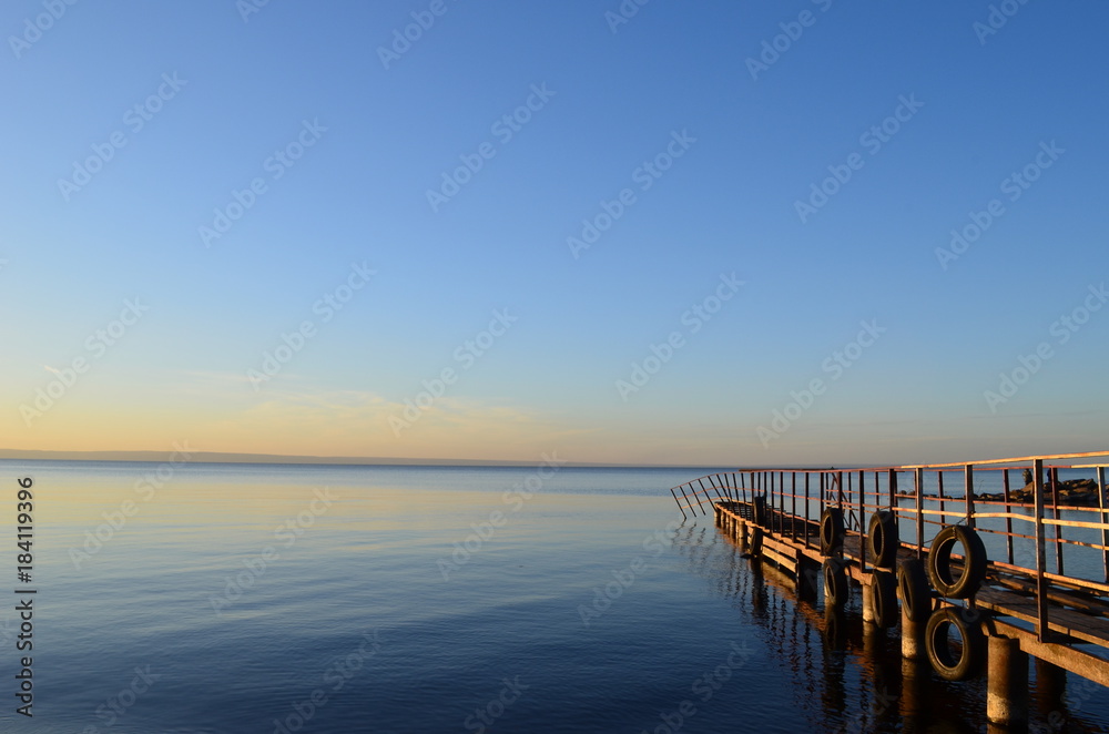 The old pier in the Volga River, lit by the sun at sunset, surrounded by water and clear sky