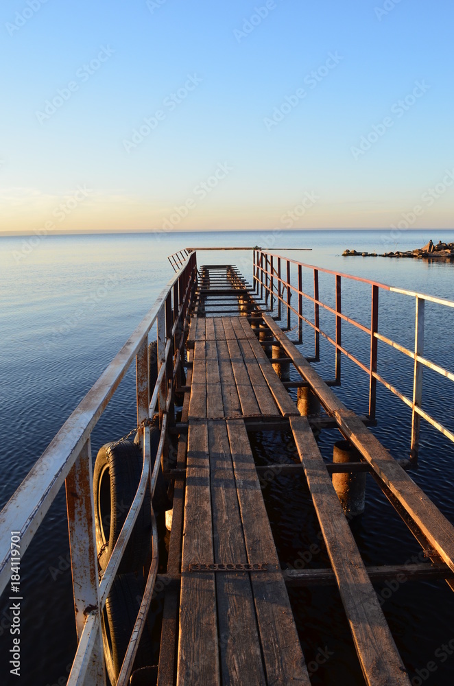 The old pier in the Volga River, lit by the sun at sunset, surrounded by water and clear sky
