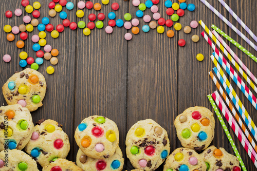 Children's cookies with colorful chocolate sweets in sugar glaze on a brown wooden background. Selective focus. Top view. Place for text.