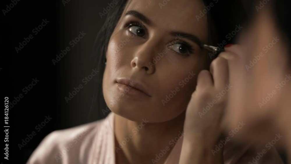 Beautiful woman painting eyebrows with mascara at mirror Beautiful woman painting eyebrows with mascara at mirror