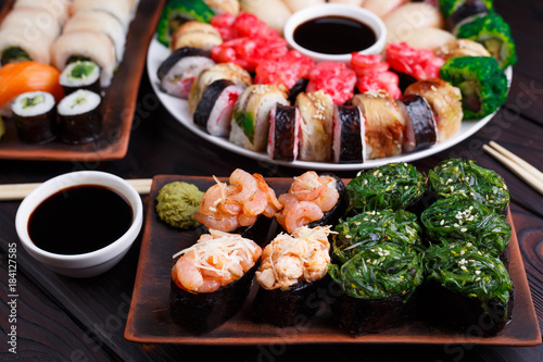 Sushi restaurant menu, Japanese food, delicious seafood concept. Great delicious set of tasty colorful sushi rolls served on the plates with soy sauce and wasabi, treats for big company