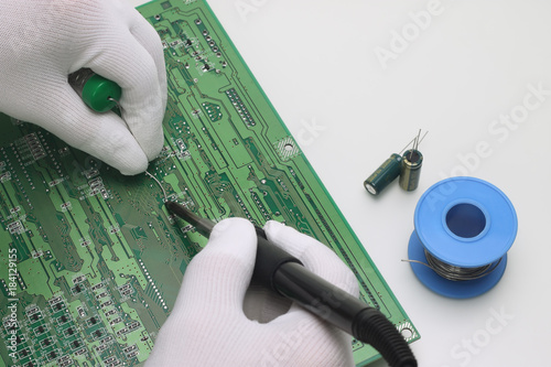 A man in antistatic gloves holding a solder and a soldering iron repairs an electronic component on a printed circuit board photo