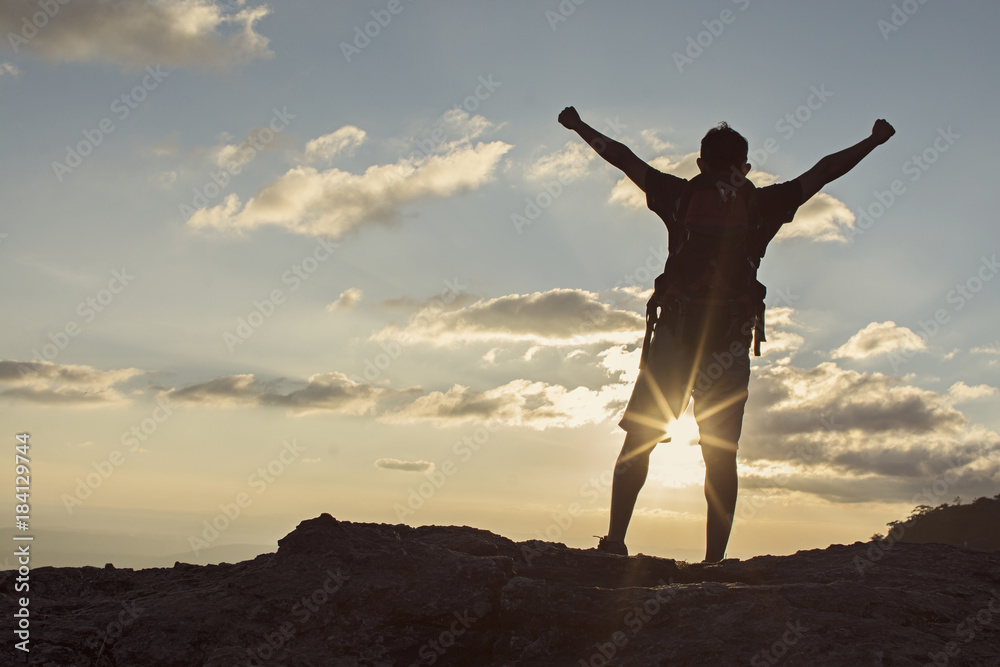 Man with backpack putting his hands up, standing on cliff