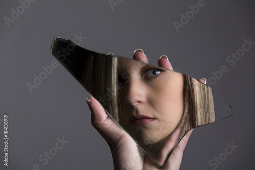 Woman looking at her face in shard of broken mirror