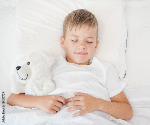 Little boy sleeping in bed with toy bear. Top view