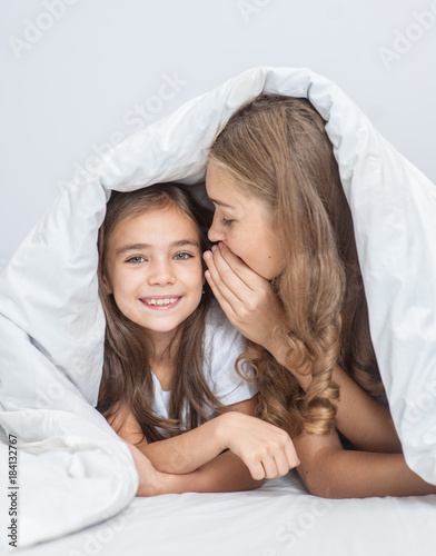 Mother and daughter sharing a secret whispering under the quilt