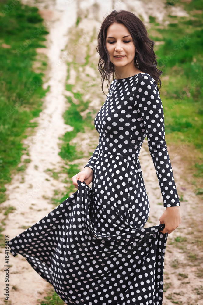 Young pretty woman with long brunette hair in vintage black dress in white peas smiling and walking on hill in nature Young pretty woman with long brunette hair in vintage black dress in white peas smiling and walking on hill in nature