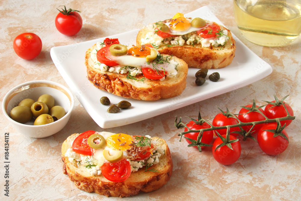 Bruschetta, crostini with cream cheese, with cherry tomatoes, herbs, olives, capers and fried egg