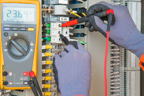 Electrician and instrument worker wearing safety gloves measuring voltage and checking electric circuit by using digital multi meter, maintenance and service job.