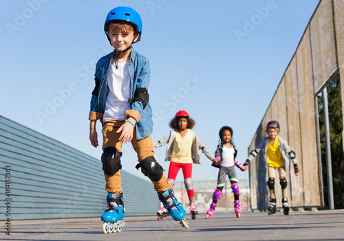Schoolboy in helmet rollerblading with his friends