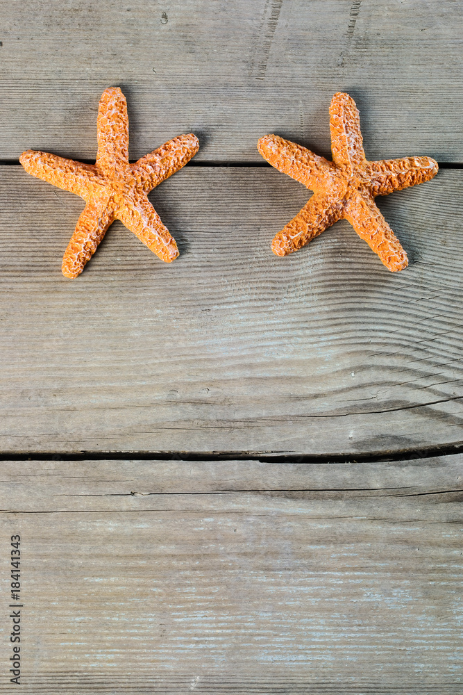 Two orange starfish lie on a gray wooden aged background of boards. Place for text. Two orange starfish lie on a gray wooden aged background of boards. Place for text.