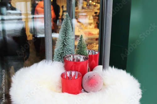 Weihnachtsdekoration (Rote Windlichter, Christbaumkugel, Tannenbäume) auf weißem Fell vor einem Geschäft. Menschen hinter Schaufenster photo